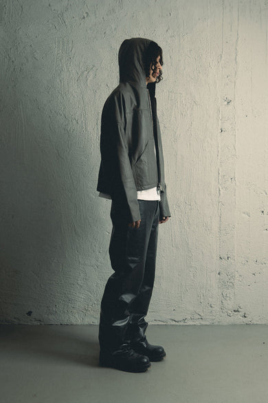 Model wearing a leather hoodie made from upcycled lambskin in black shot in profile. It features duo front pockets, zipper closure, a cozy hood, and a drawstring at the bottom hem.