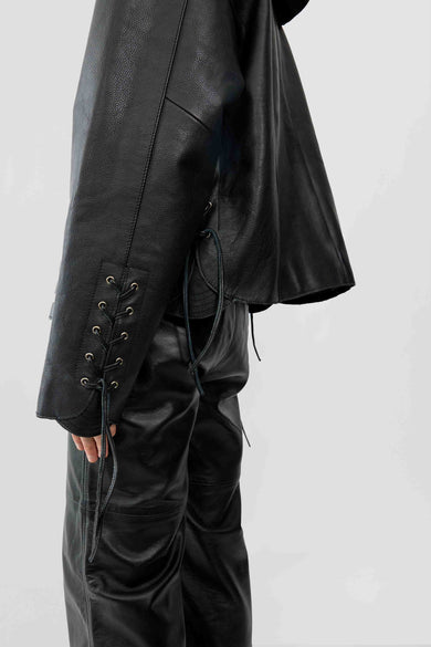 Close up of model wearing Canoo Jacket in black upcycled leather, featuring drawstrings in cufs and duo waist pockets.