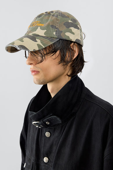 Model wearing Carpe Diem baseball cap in camo made out of recycled cotton, featuring an orange embroidery and a silver-tone buckle in the back