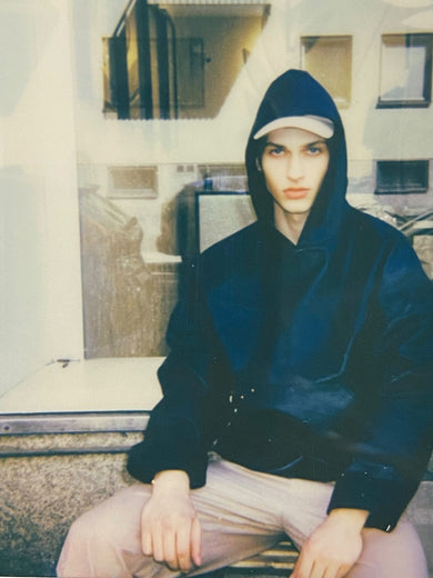 Model wearing hoodie in upcycled black leather and carpe diem cap outside Deadwood store.