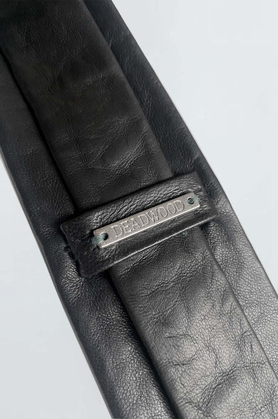 Close up of backside of Timo Tie by Deadwood. Black leather tie made from upcycled lambskin with silver-tone logo detail.